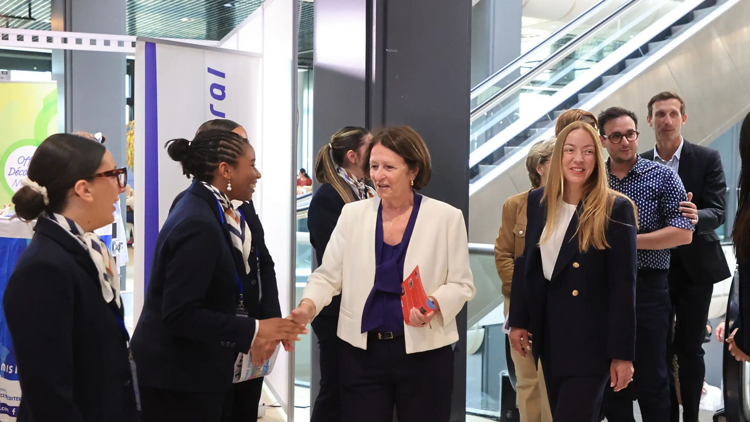 Une femme en blazer blanc serre la main d'une professionnelle en uniforme bleu marine.