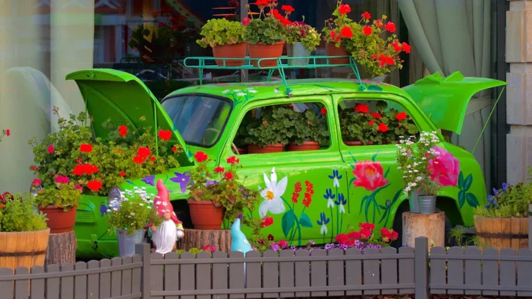 Une voiture verte ancienne transformée en jardinière artistique avec des fleurs rouges et des nains de jardin.