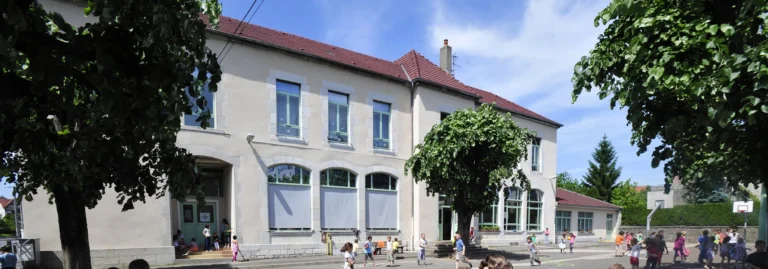 Enfants jouant dans la cour d'une école primaire devant un grand bâtiment en pierre clair.
