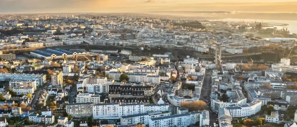 Vue aérienne panoramique d'une ville dense aux immeubles blancs baignée par la lumière du soleil couchant.