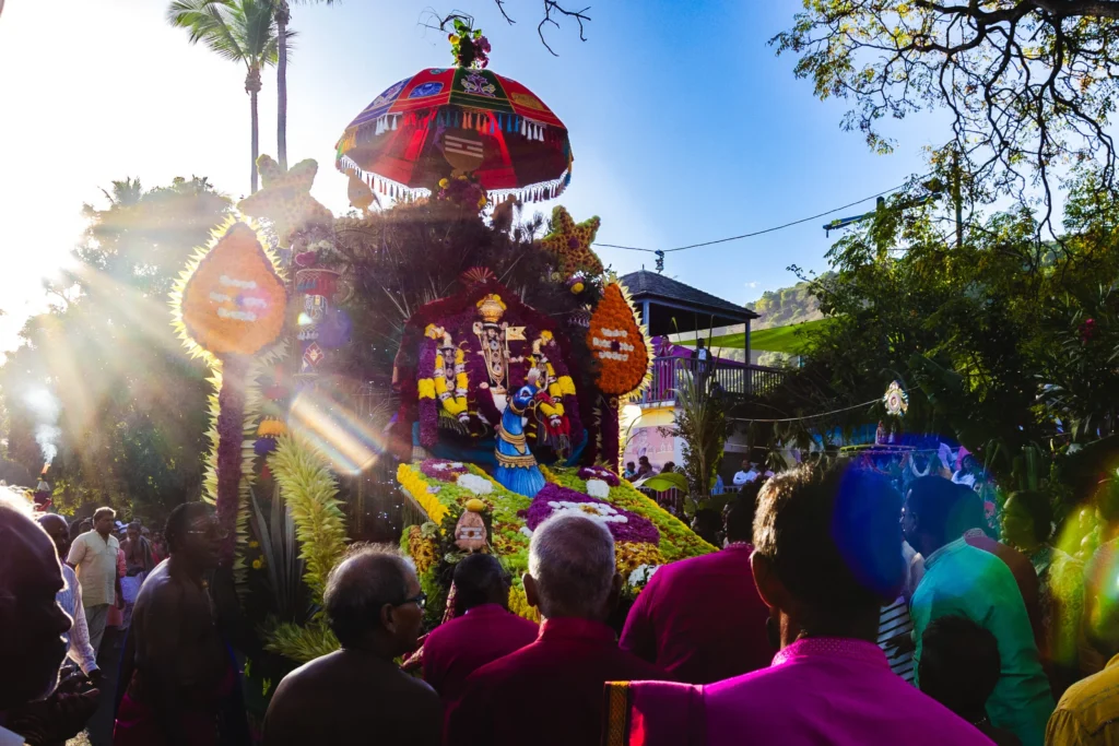 Grand char hindou coloré orné de fleurs et d'un parasol, entouré d'une foule de fidèles.