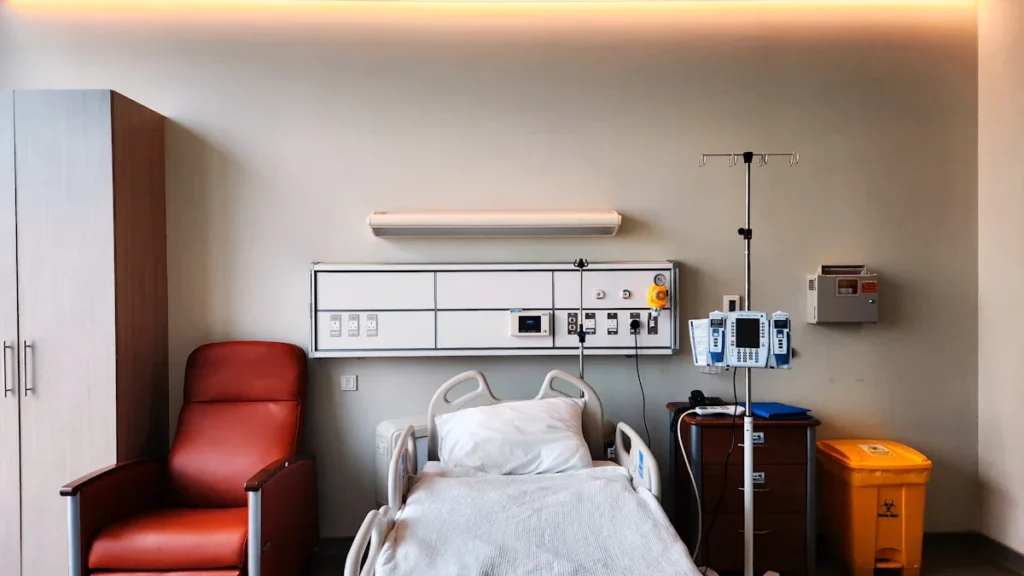 Une chambre d'hôpital individuelle moderne avec un lit médicalisé, un fauteuil et un éclairage design.