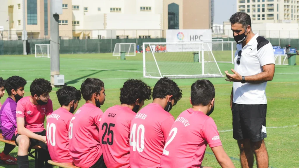 Un entraîneur de football s'adressant à une rangée de jeunes joueurs sur un terrain de sport.