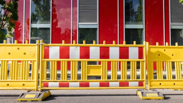 Barrières de sécurité jaunes et rouges installées devant un bâtiment moderne pour délimiter le parcours.