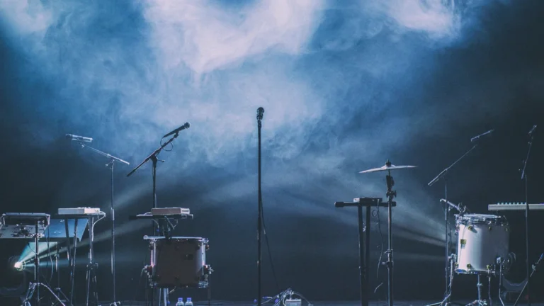 Une scène de concert extérieure avec batterie et microphones sous des projecteurs et de la brume.