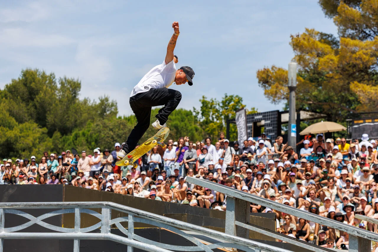 Skateur en plein saut au-dessus d'une rampe métallique devant une foule dense lors d'une compétition.