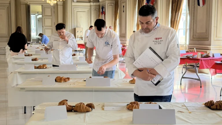 Des boulangers en vestes blanches évaluent des croissants sur des tables lors d'un concours officiel.
