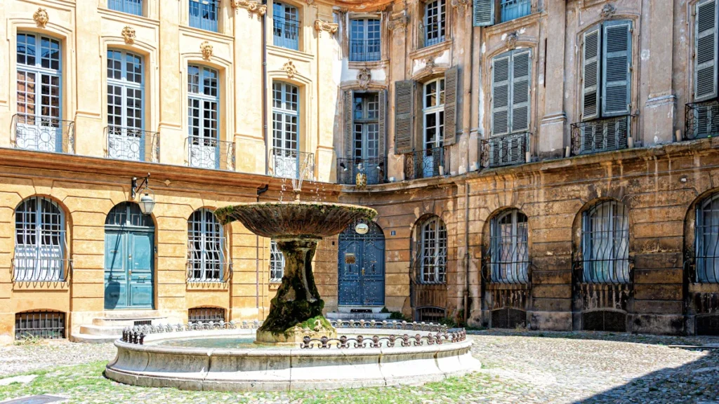 Une fontaine ancienne au centre d'une cour pavée entourée de bâtiments historiques à Aix-en-Provence.