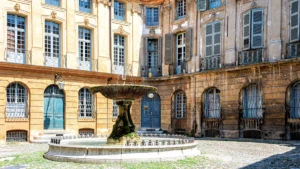 Une fontaine ancienne au centre d'une cour pavée entourée de bâtiments historiques à Aix-en-Provence.