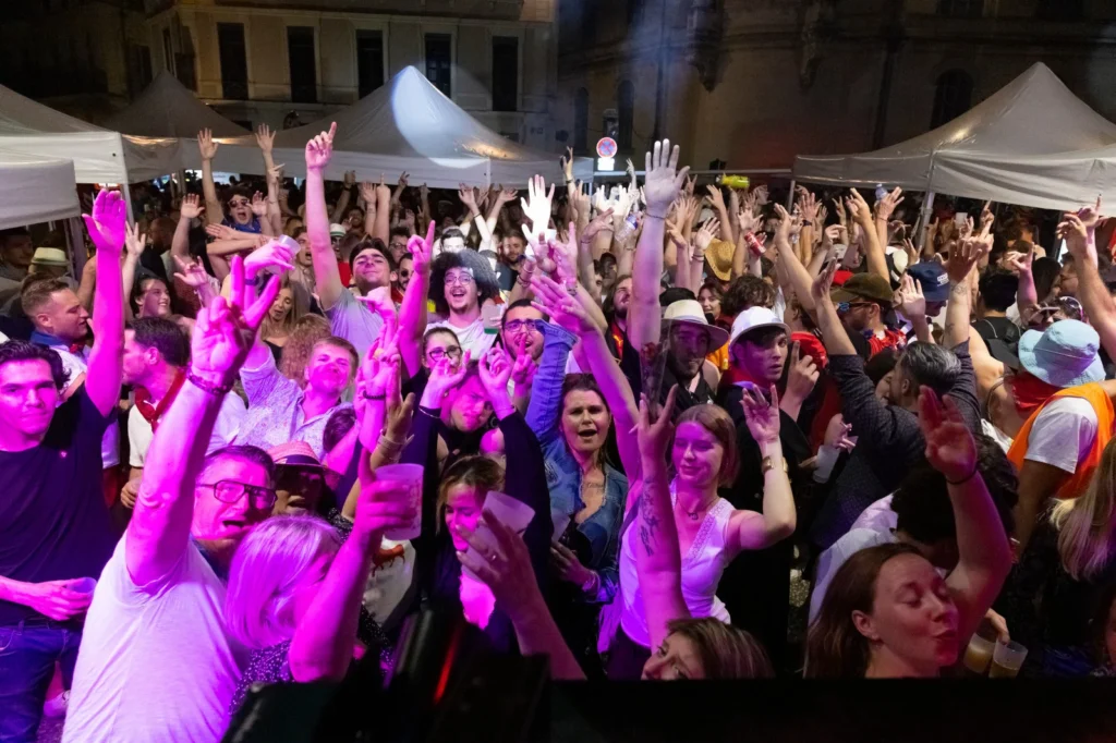 Foule dense levant les mains lors d'un événement festif nocturne sous des tentes blanches éclairées.