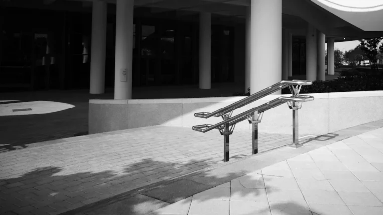 Une rampe d'accès pour personnes à mobilité réduite avec double main courante devant un bâtiment moderne.