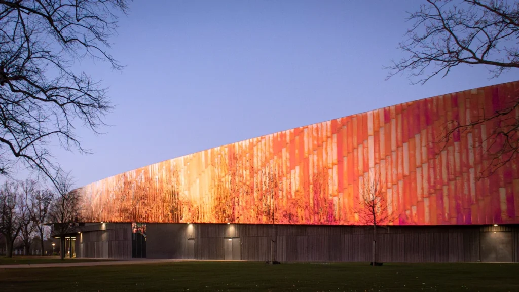 Façade moderne aux tons cuivrés d'un complexe sportif entouré de verdure au coucher du soleil.