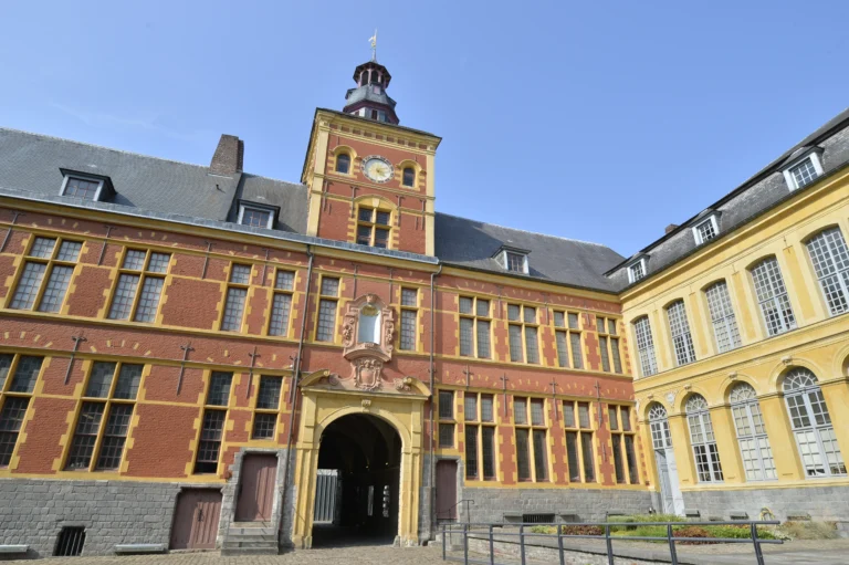 Bâtiment historique en briques rouges et pierres jaunes avec une tour d'horloge centrale.