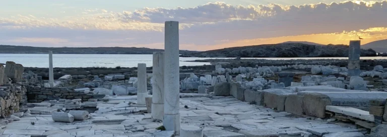 Vestiges de colonnes en marbre blanc face à la mer sous un ciel de coucher de soleil.