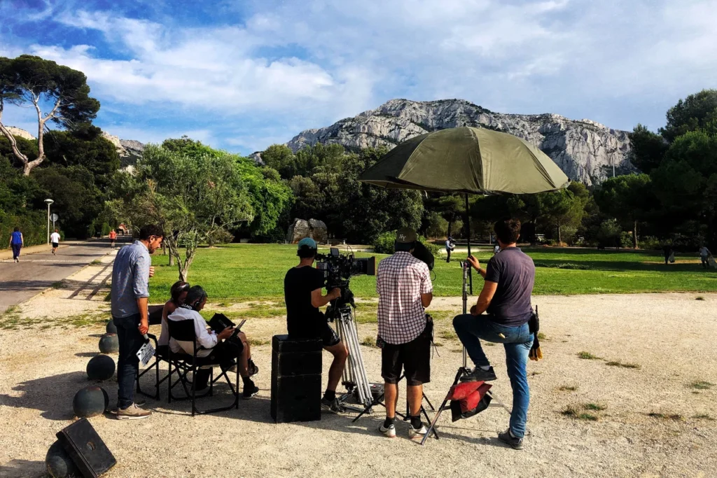 Équipe de tournage avec caméra et matériel devant une montagne rocheuse dans un parc ensoleillé.