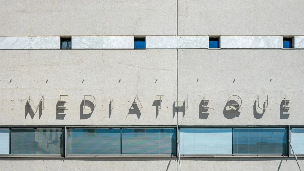 Détail architectural de la façade en béton d'une médiathèque moderne avec le mot 'MEDIATHEQUE' inscrit en lettres capitales créant des ombres portées.