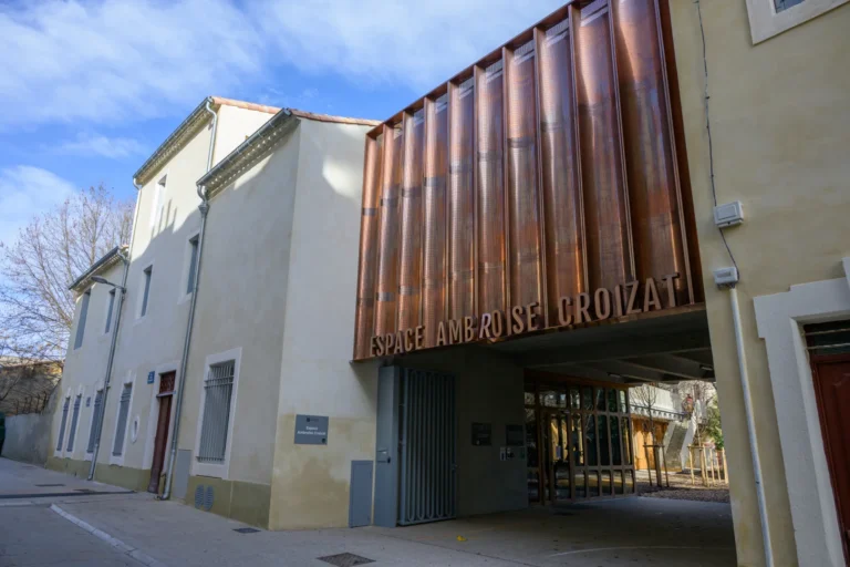 Façade moderne de l'Espace Ambroise Croizat avec panneaux métalliques cuivrés et murs clairs.