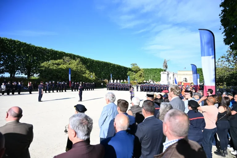 Des pompiers en uniforme alignés lors d'une cérémonie officielle devant une foule de spectateurs.