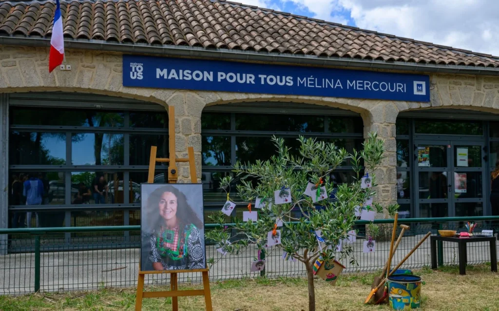 Façade de la Maison Mélina Mercouri avec un portrait sur chevalet et un olivier décoré.