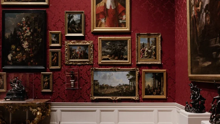Plusieurs tableaux de maîtres exposés sur un mur rouge damassé dans une galerie d'art classique.