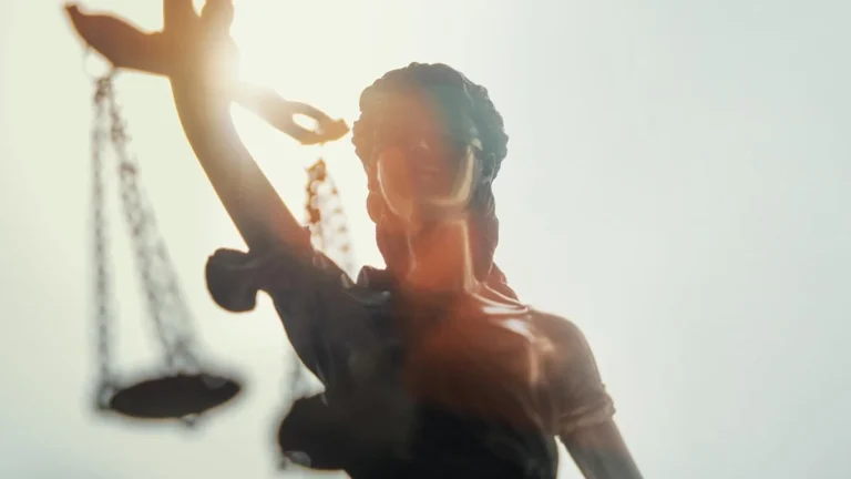 Statue de la Justice aux yeux bandés tenant une balance sous une lumière éclatante.