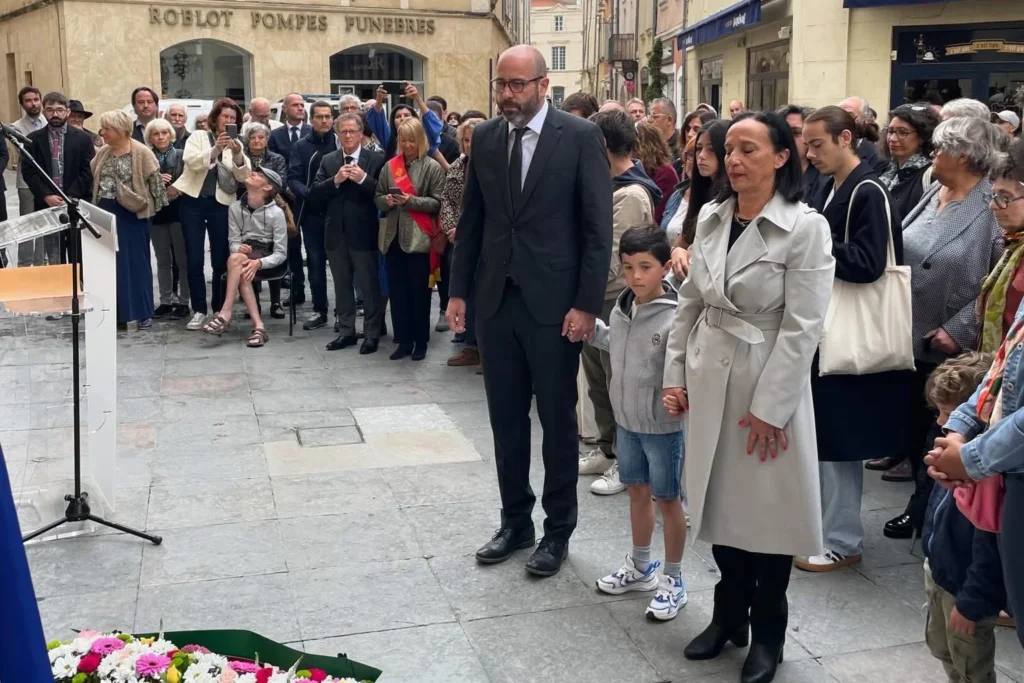 Un homme, un jeune garçon et une femme se tiennent la main devant une foule recueillie.