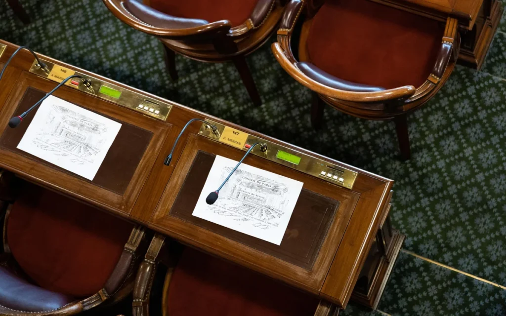 Vue plongeante de deux bureaux en bois du Conseil de Paris avec microphones et documents.