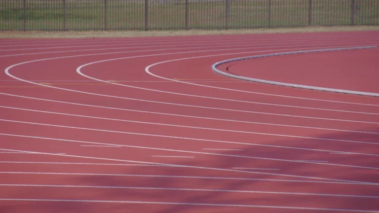 Vue en angle d'une piste d'athlétisme rouge aux lignes blanches sinueuses dans un parc sportif.