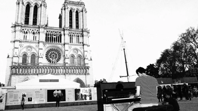 Un pianiste joue sur une place publique française devant la façade d'une grande cathédrale.