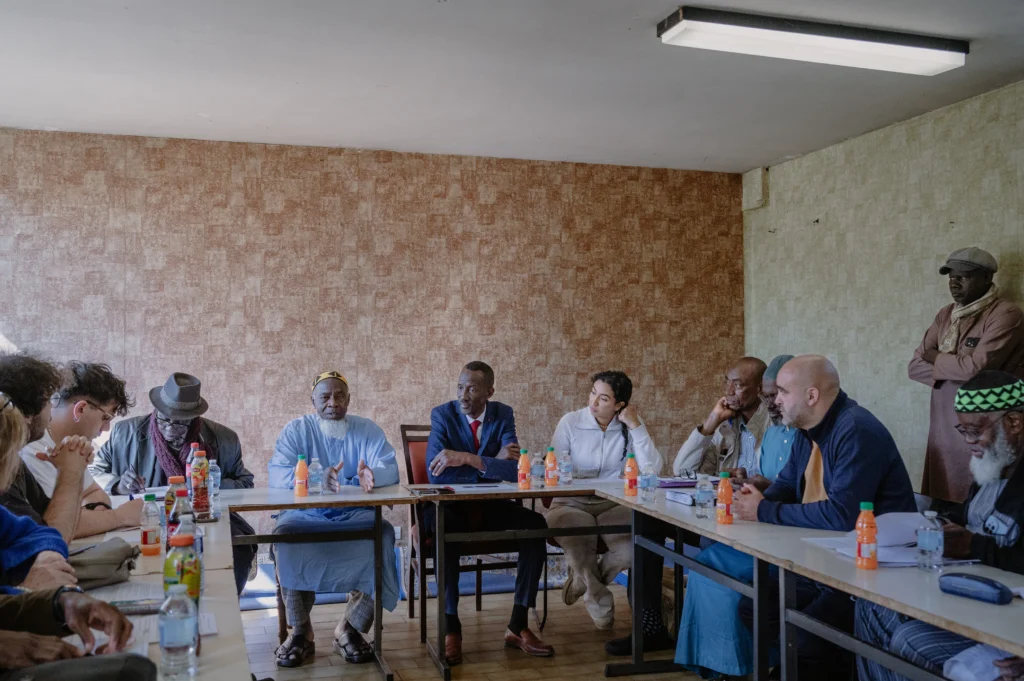 Groupe de personnes d'origines diverses discutant autour d'une table lors d'une réunion formelle en intérieur.