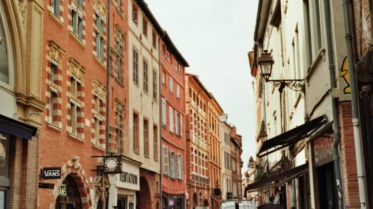 Perspective d'une rue typique de Toulouse avec ses façades historiques en briques rouges et des passants.