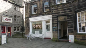 Façade en pierre d'un café convivial accueillant des visiteurs en terrasse extérieure.