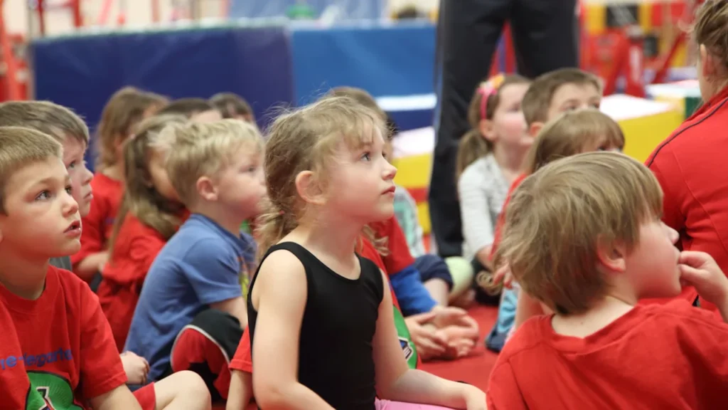 Groupe d'enfants assis attentivement lors d'une activité sportive en salle