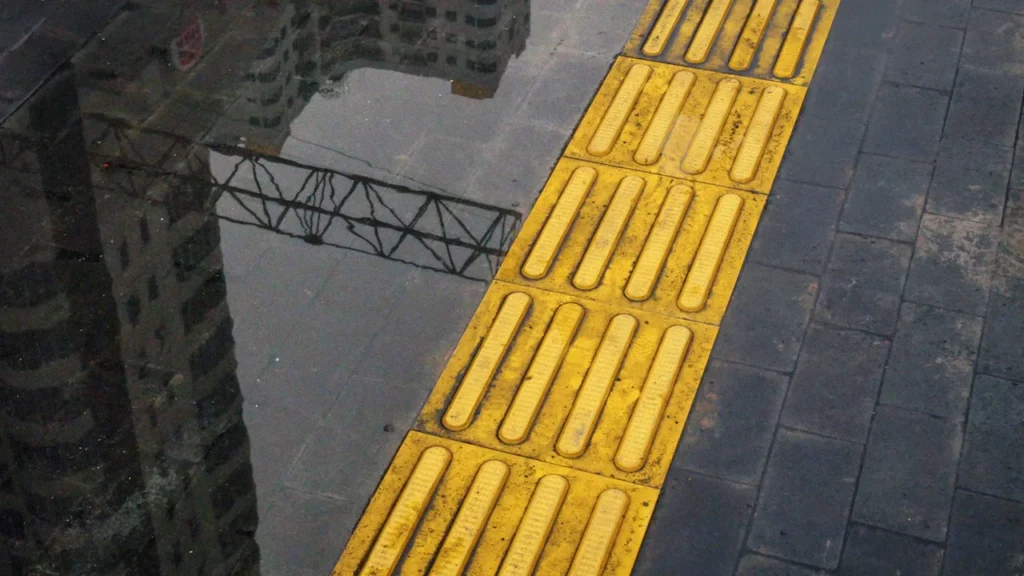 Dalle podotactile jaune sur un trottoir urbain pour guider les personnes non-voyantes.