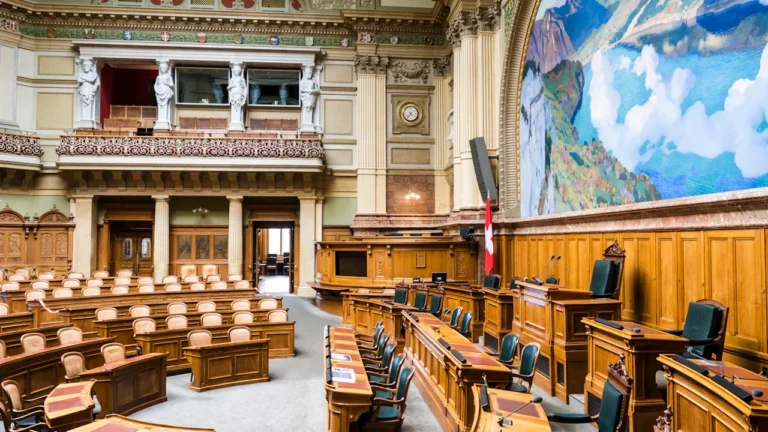 Vue intérieure d'une salle de conseil parlementaire avec des bancs en bois classiques.