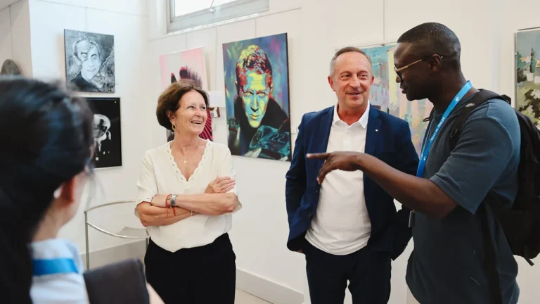 Trois personnes discutent et sourient devant des tableaux colorés dans une galerie d'art moderne.
