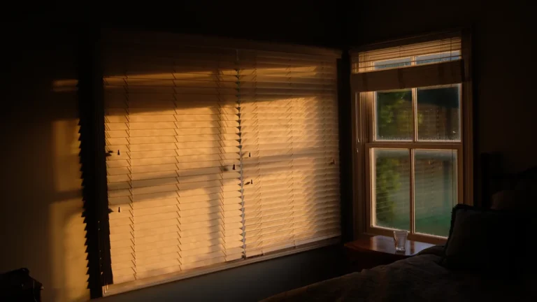 Lumière du soleil couchant filtrée à travers des stores baissés dans une chambre.