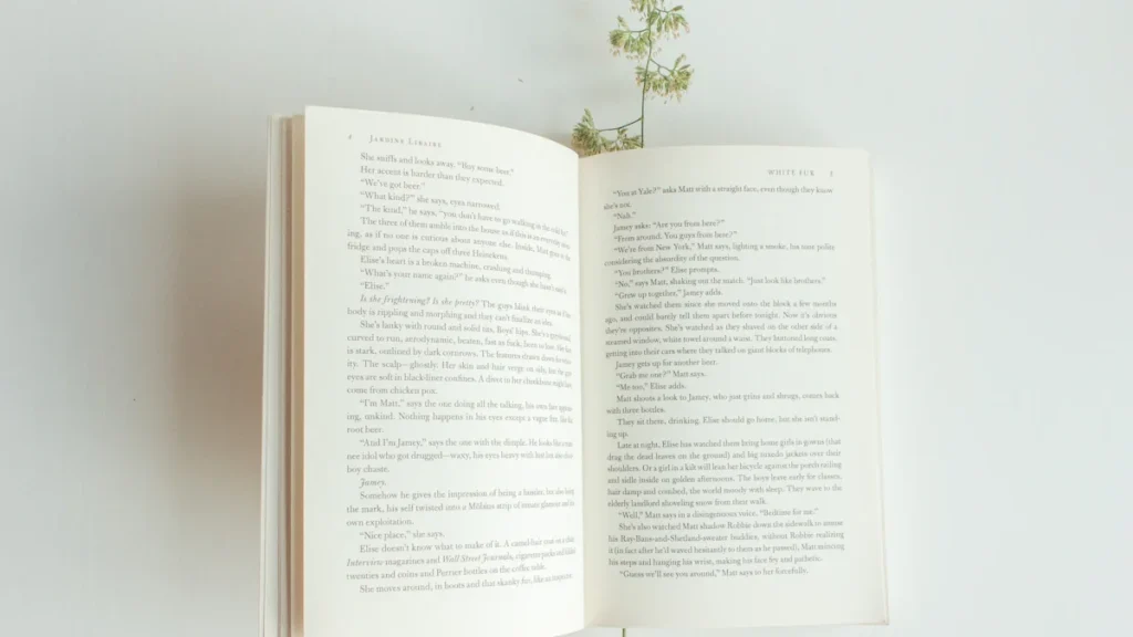 Un livre ouvert posé sur une table avec une plante verte délicate.