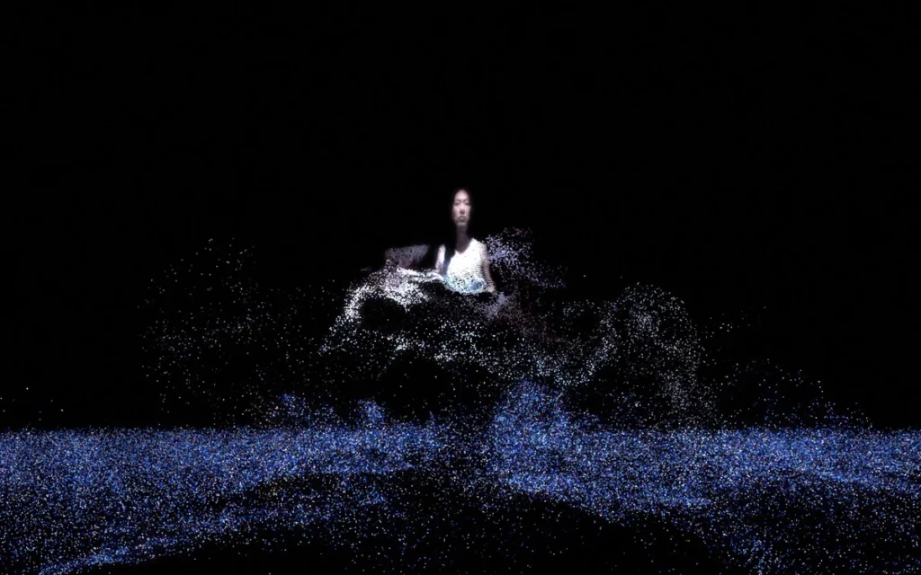 Une personne émerge de particules lumineuses bleues et blanches dans un espace sombre.