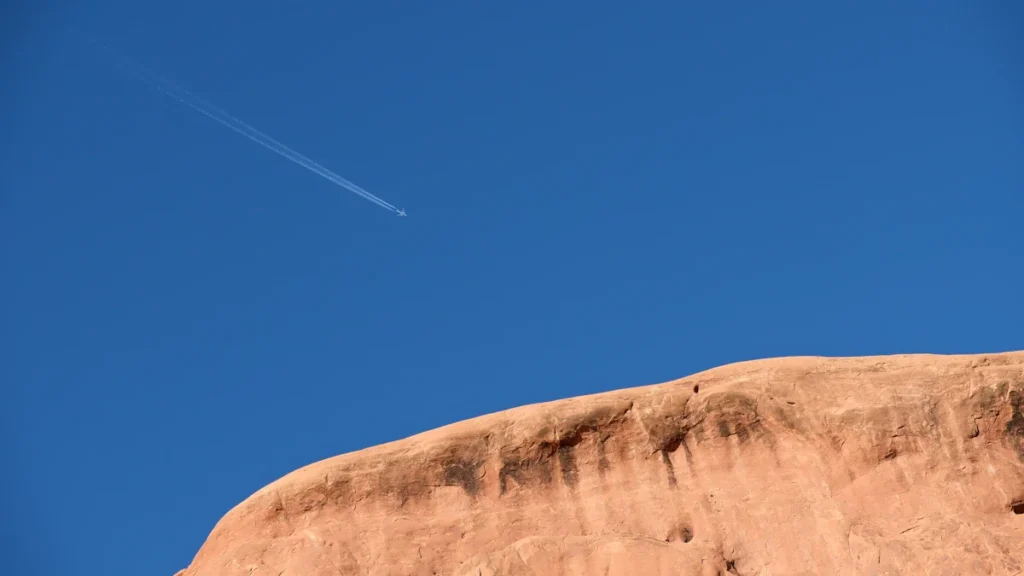 Un avion laissant une traînée blanche dans un ciel bleu dégagé au-dessus des rochers.
