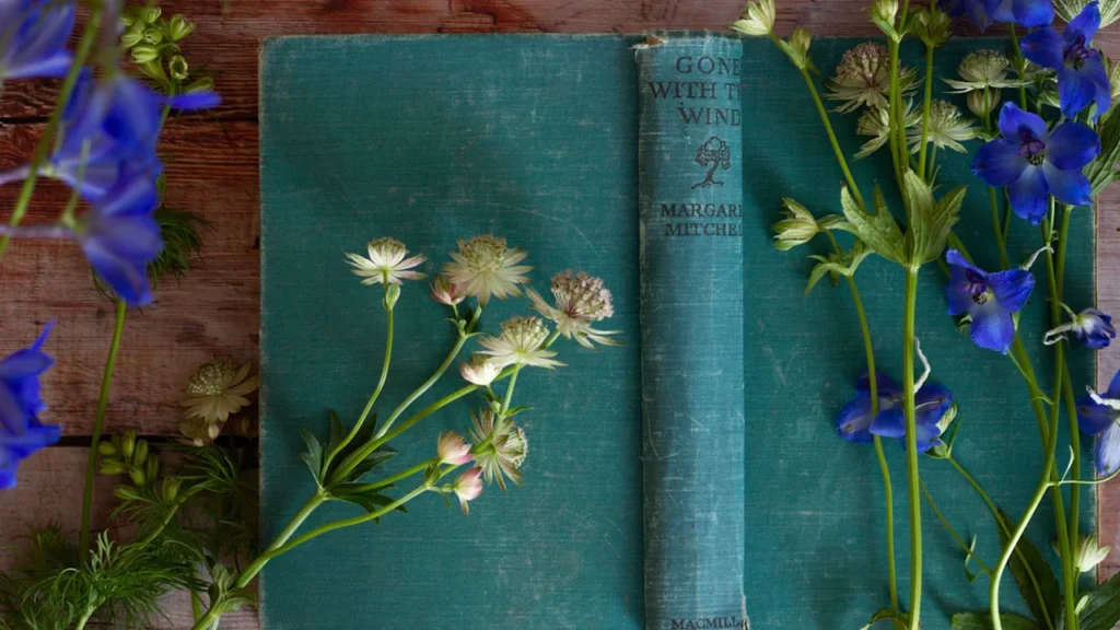 Livre ancien posé avec des fleurs bleues évoquant le jardin de Candide.