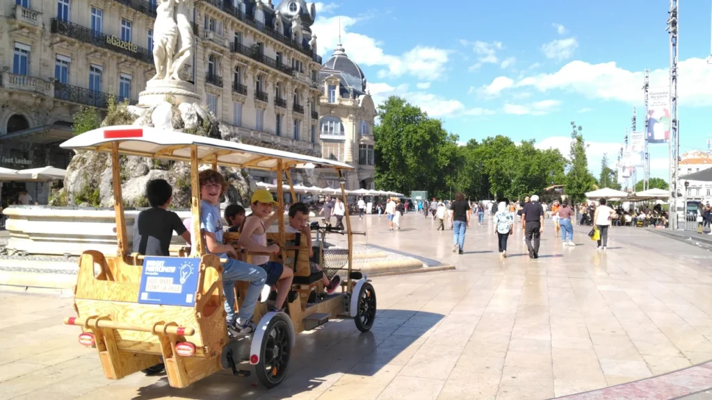 Un groupe d'enfants s'amuse sur un vélo-taxi en bois place de la Comédie, Montpellier.