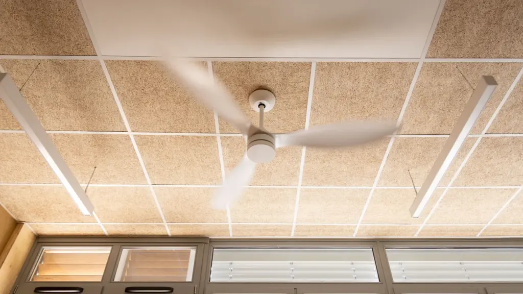 Un ventilateur de plafond blanc en mouvement sous un plafond en panneaux de bois.