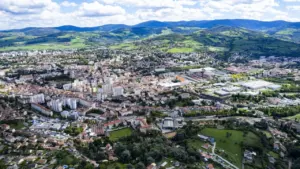 Vue aérienne panoramique d'une ville française nichée au pied de montagnes verdoyantes en été.