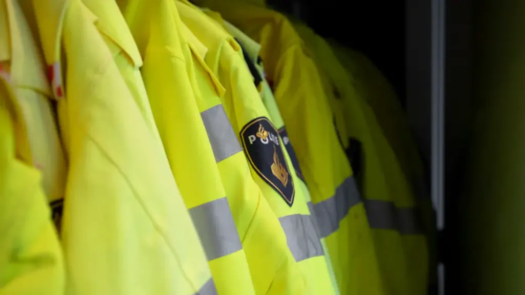 Plusieurs vestes de sécurité jaune fluo suspendues sur un cintre dans une pénombre.