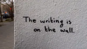 Graffiti sur un mur urbain avec l'inscription en anglais : The writing is on the wall.