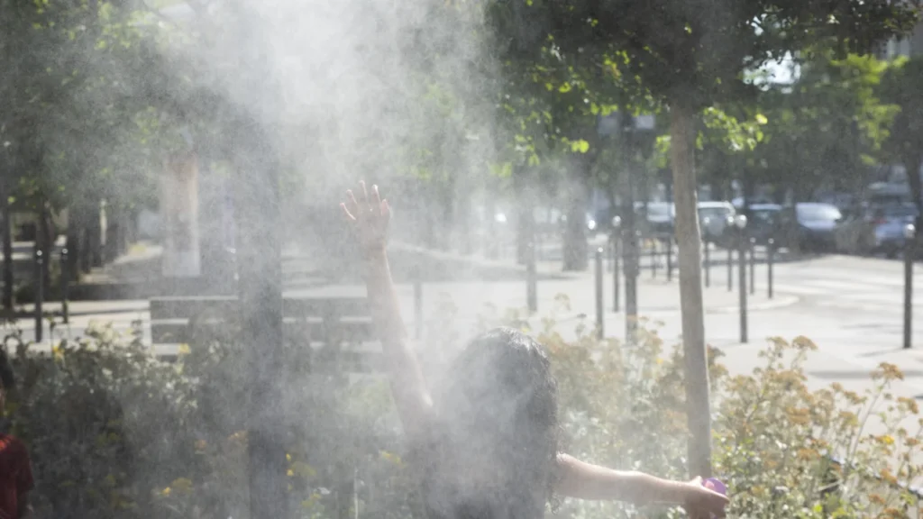 Une personne de dos lève les bras dans une fine brume rafraîchissante en extérieur.