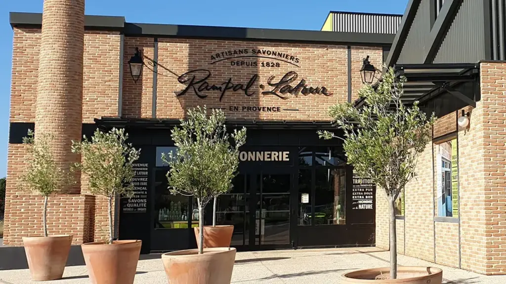 Façade en briques d'une savonnerie artisanale provençale avec des oliviers en pots devant l'entrée.