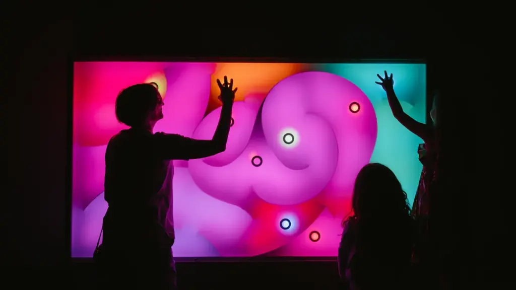 Silhouettes de visiteurs interagissant avec un écran numérique interactif et coloré.