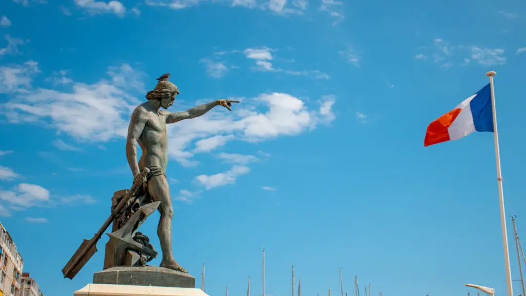 Statue marine au port de Toulon sous un ciel bleu avec drapeau français flottant.